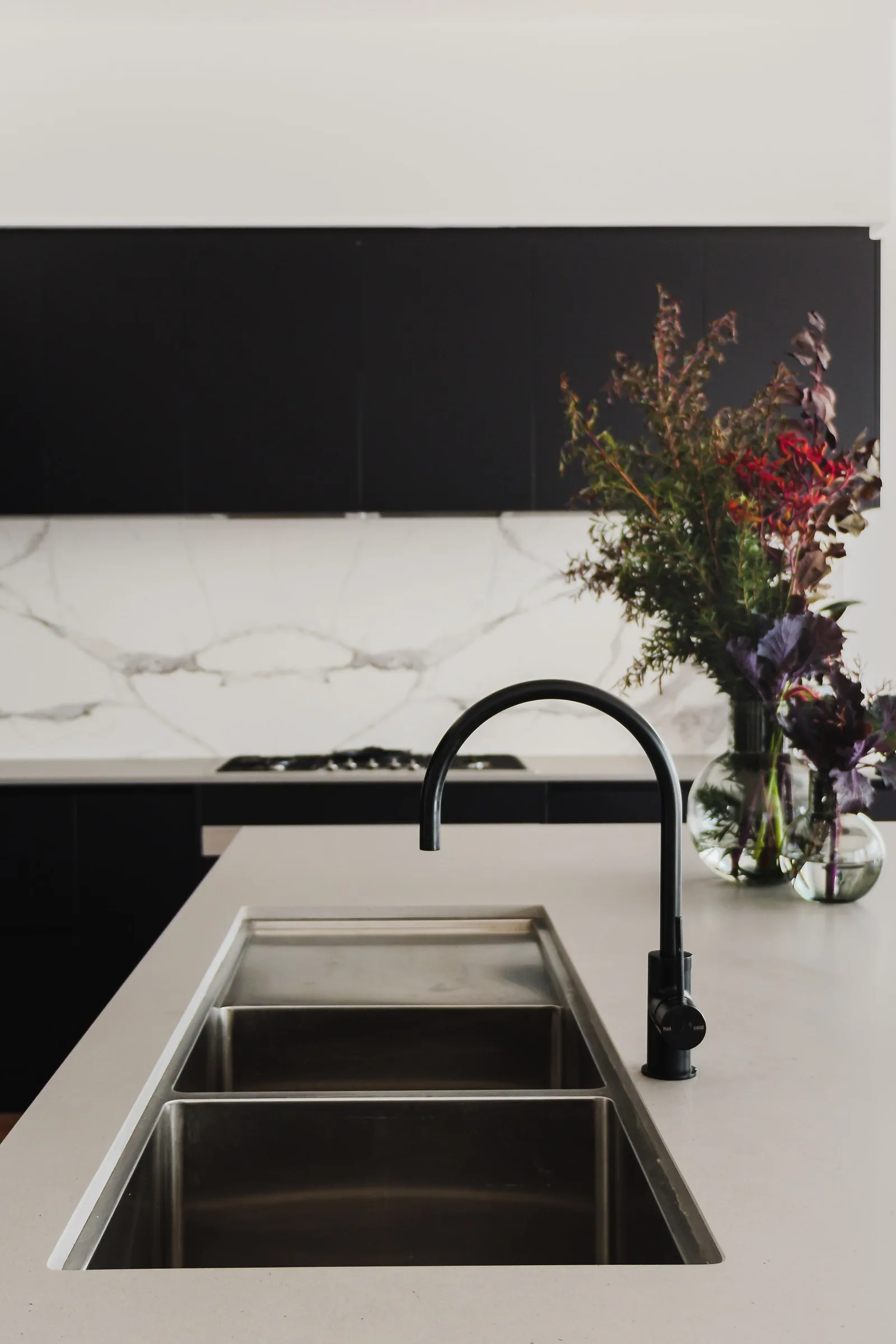 Black kitchen tapware over a pale stone island, with charcoal cabinetry and veined stone beyond